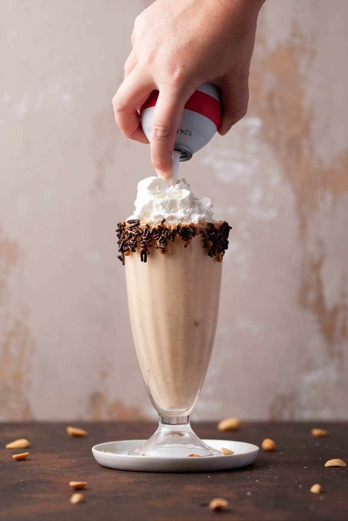 Adding whipped cream topping to a peanut butter milkshake.