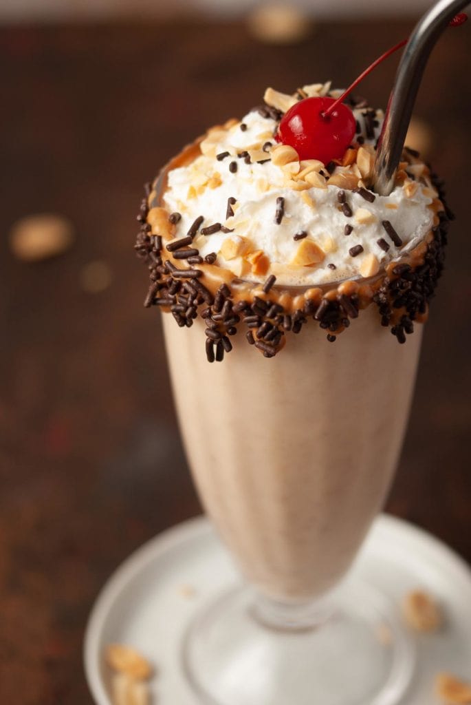 45 degree angle close up of a peanut butter milkshake with whipped cream and a cherry on top