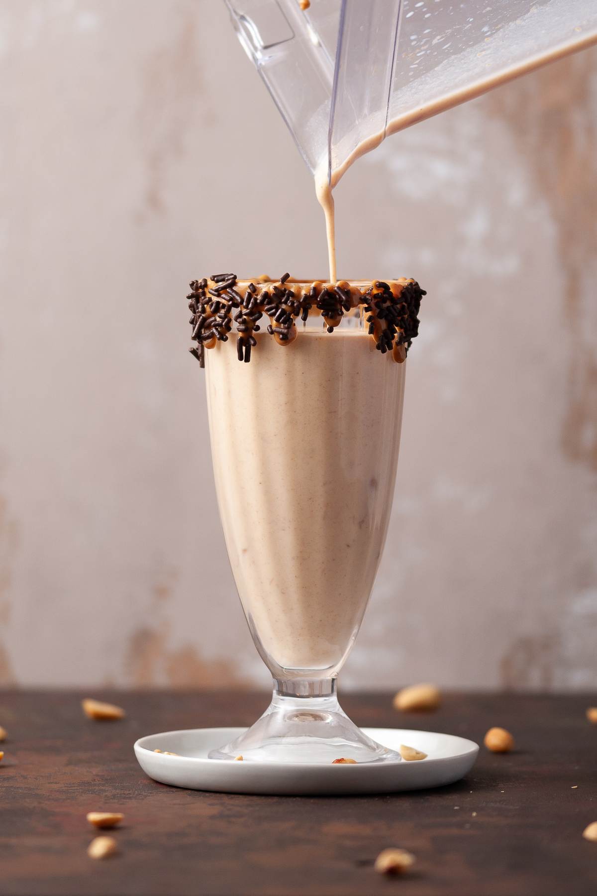 Peanut butter milkshake being poured from a blender into a glass.