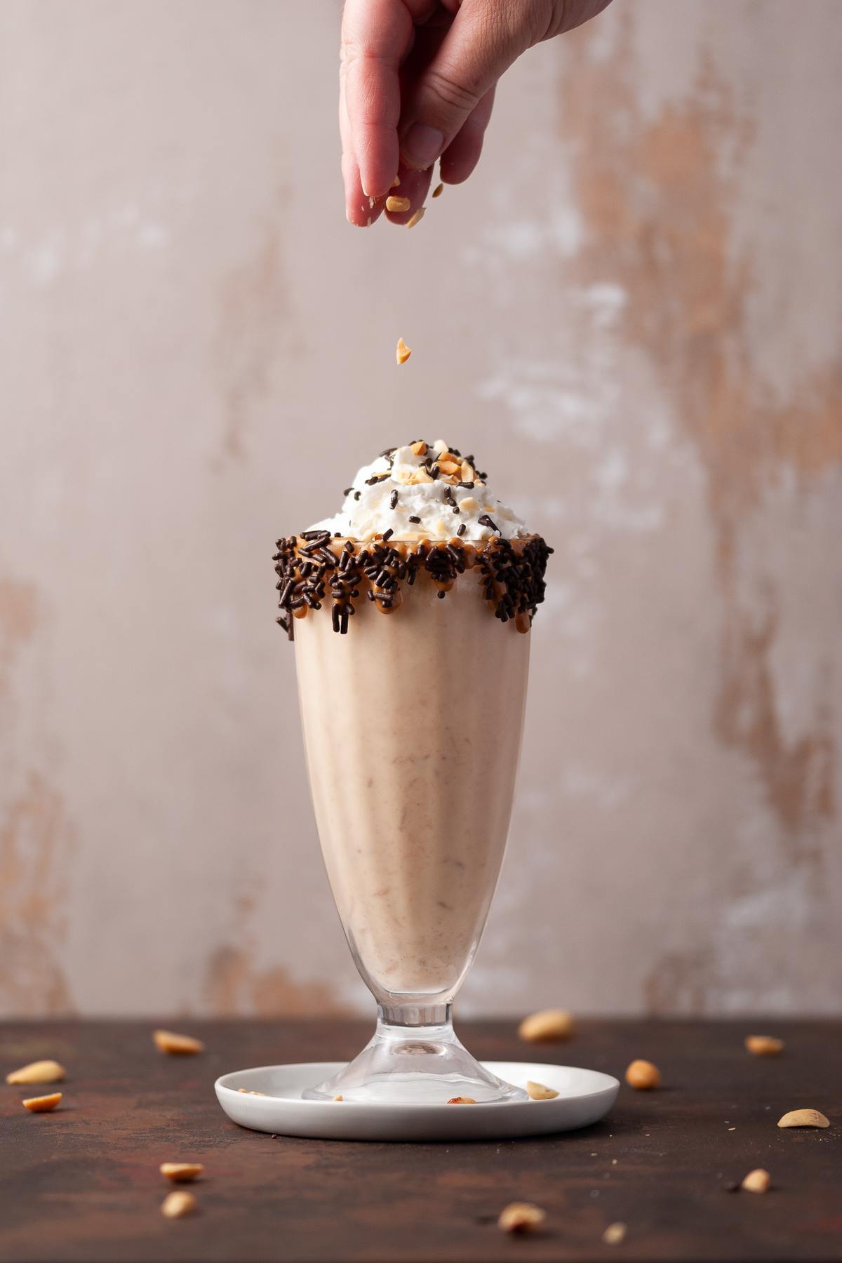 Adding peanuts to the top of a peanut butter milkshake.