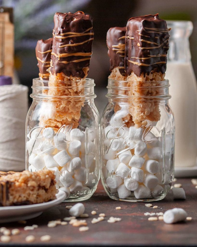 mason jar filled with marshmallows and two chocolate and peanut butter covered rice krispie treats