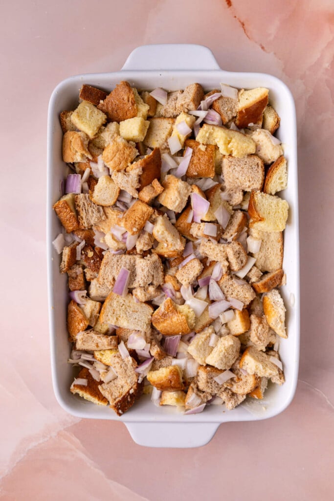 Casserole dish layered with butter, bread, and a seasoned egg wash with shallots. 