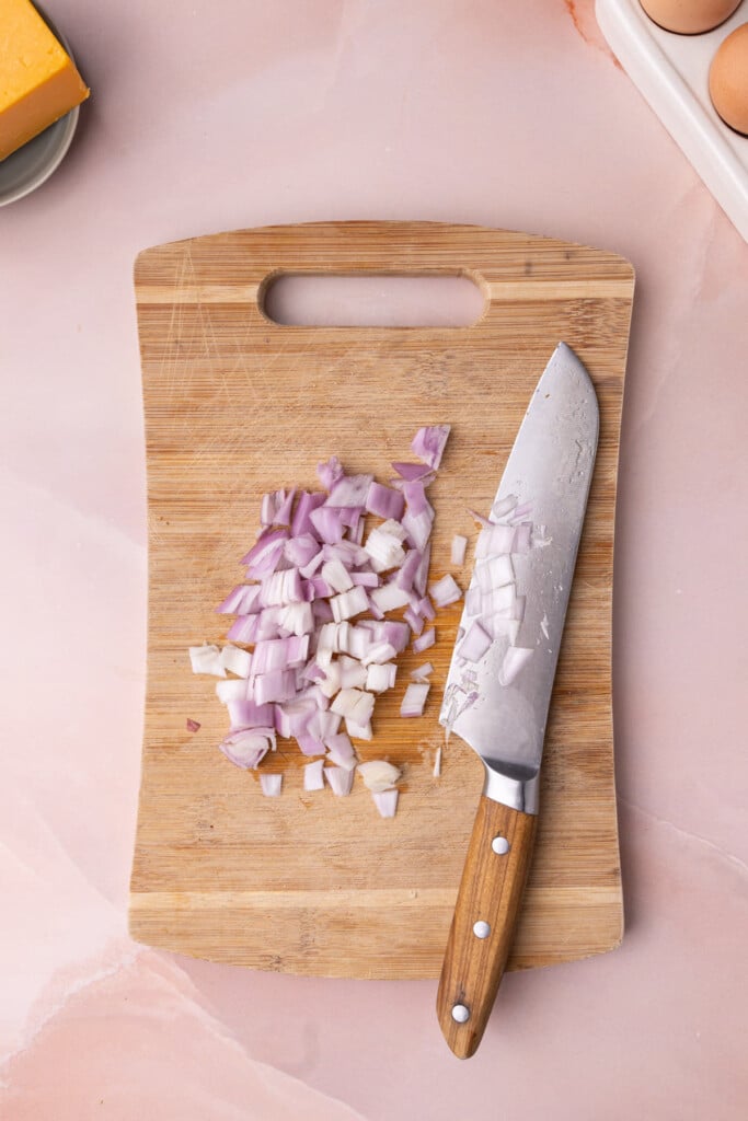Diced shallot on a wooden cutting board with a sharp knife. 