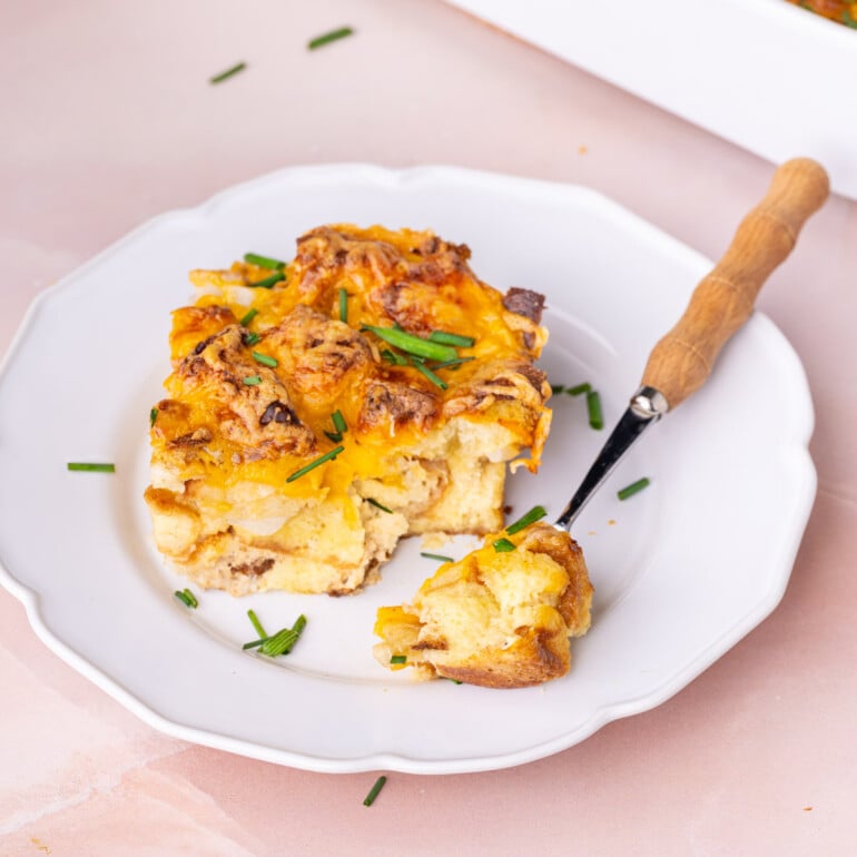 Thick slice of savory breakfast casserole on a white plate with a forkful off to the side.