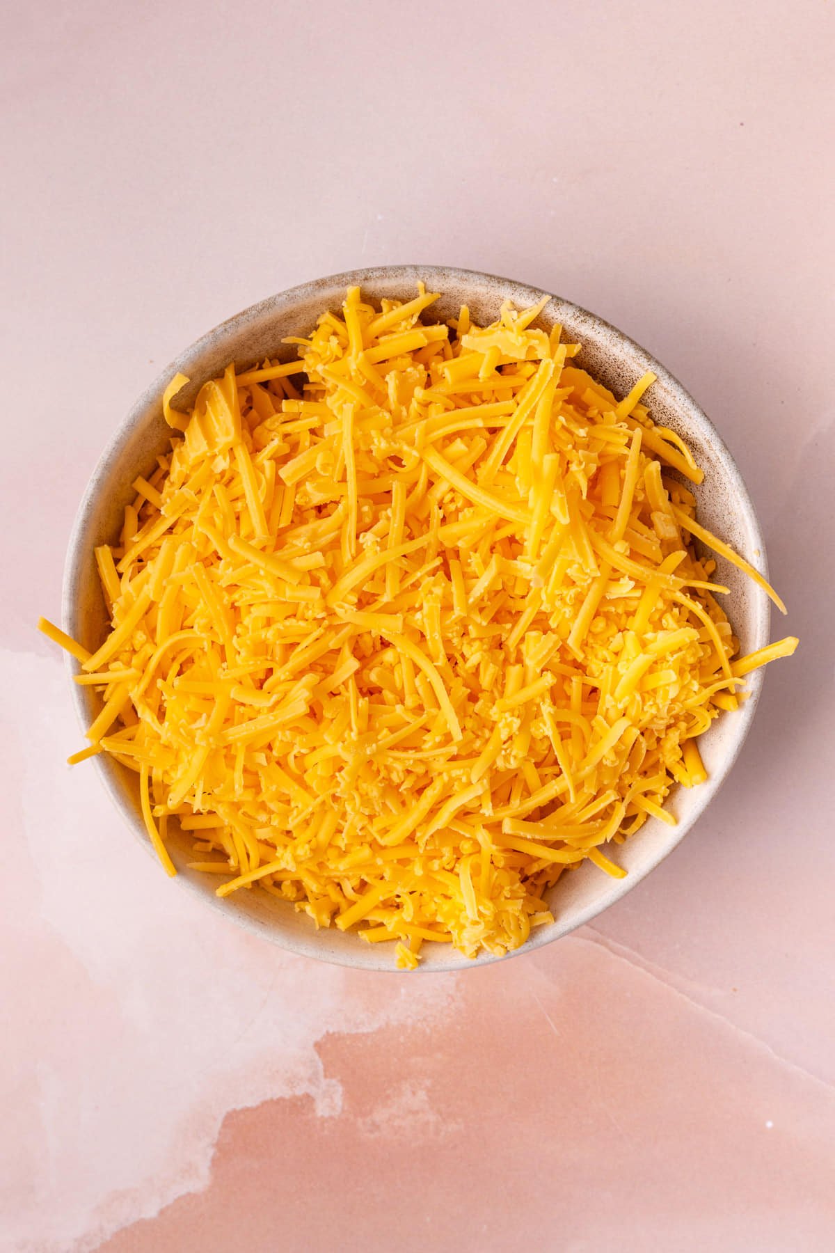Cheddar cheese that has been hand shredded from a block of cheese in a bowl. 