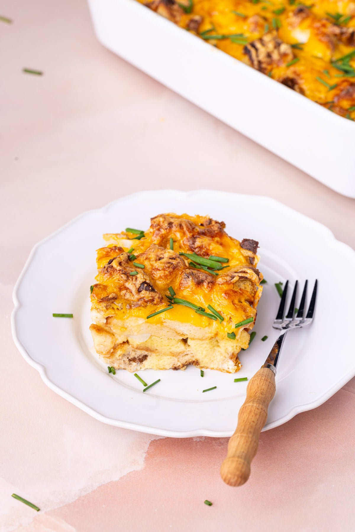 Generous portion of savory French toast casserole on a white plate peppered with chives. 