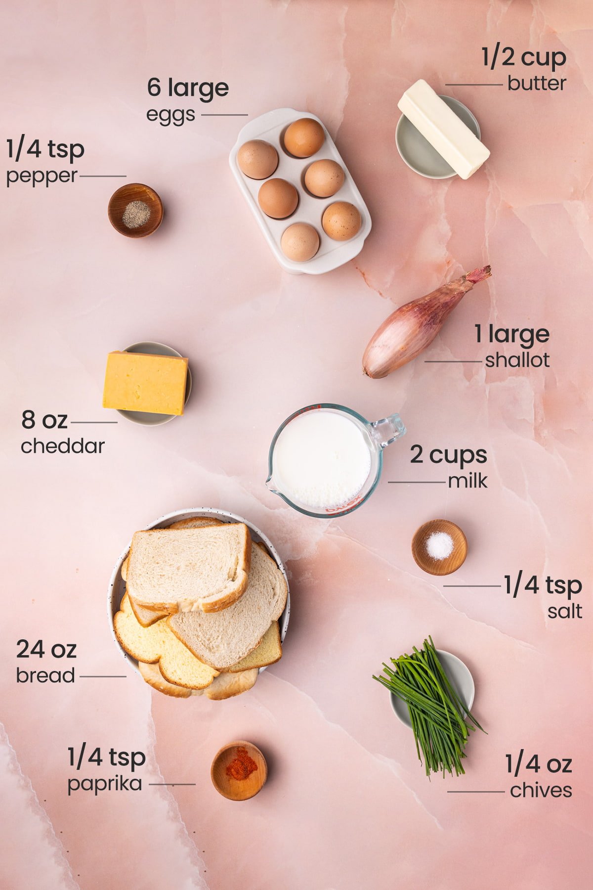 Overhead view of all the ingredients needed for savory French toast casserole - eggs, butter, pepper, shallot, cheddar, milk, salt, bread, paprika, and chives.