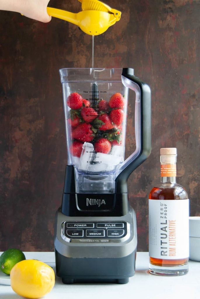 squeezing citrus juice into a blender with strawberries and ice