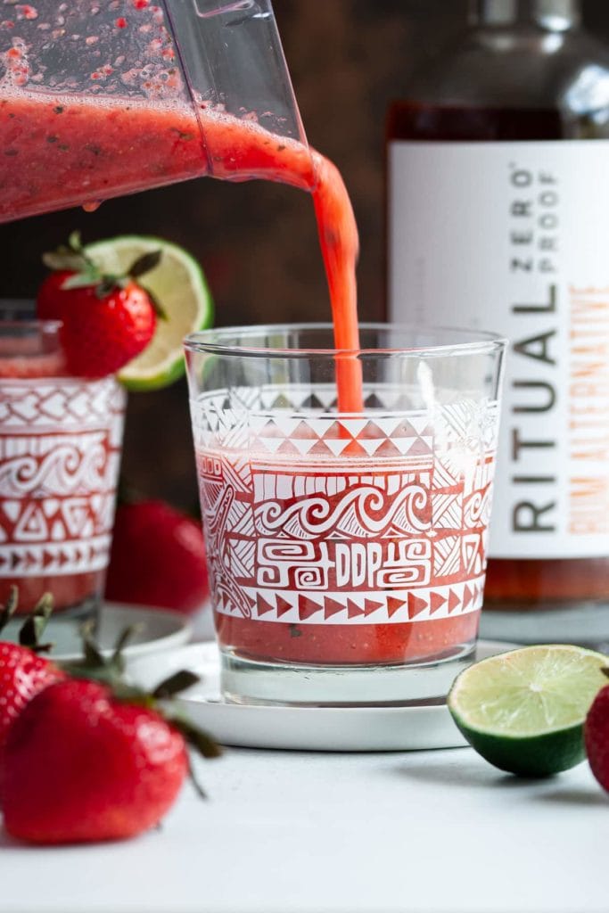 Pouring strawberry daiquiri mocktail with rum alternative into a decorative glass