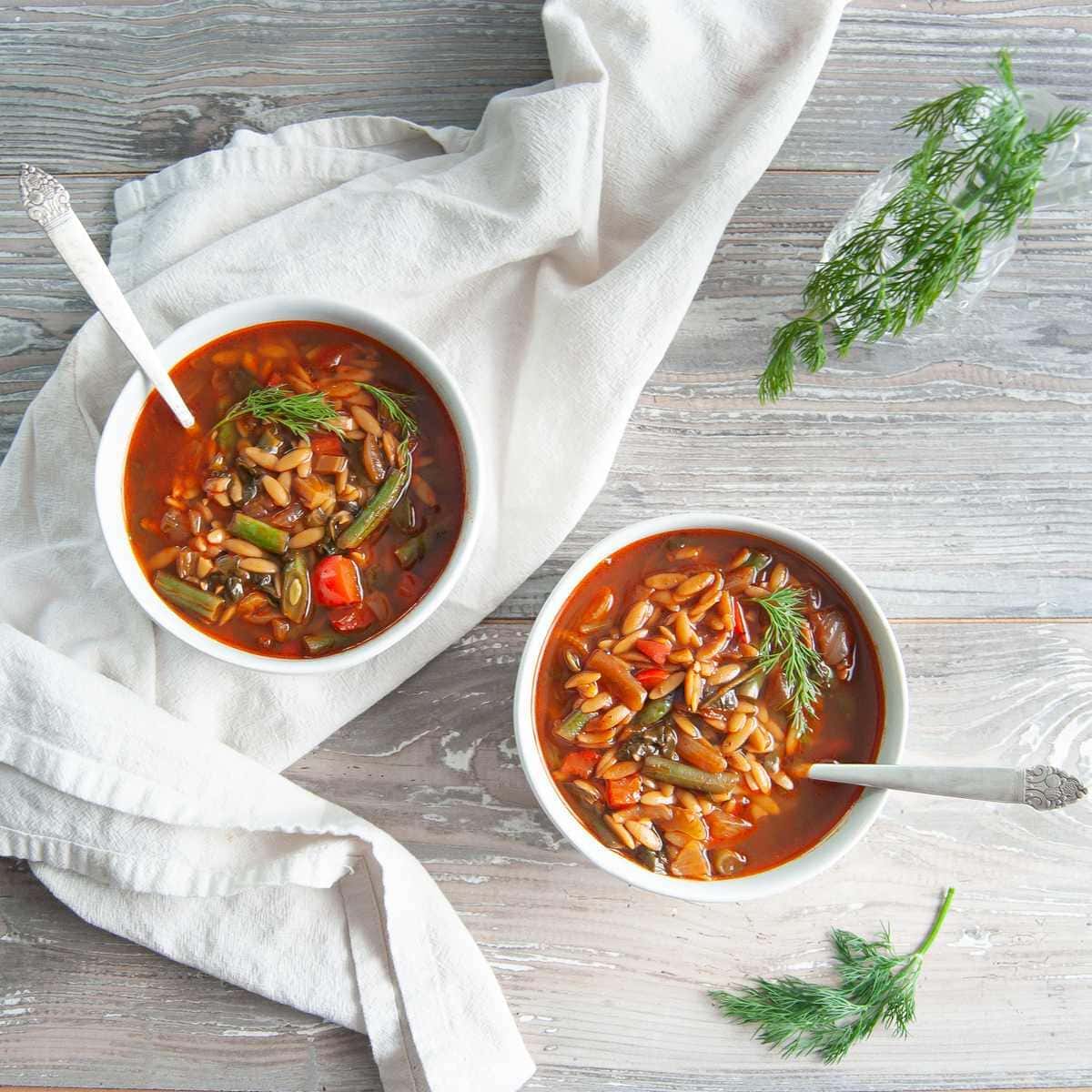 Two bowls of vegetable soup with orzo on kitchen towel