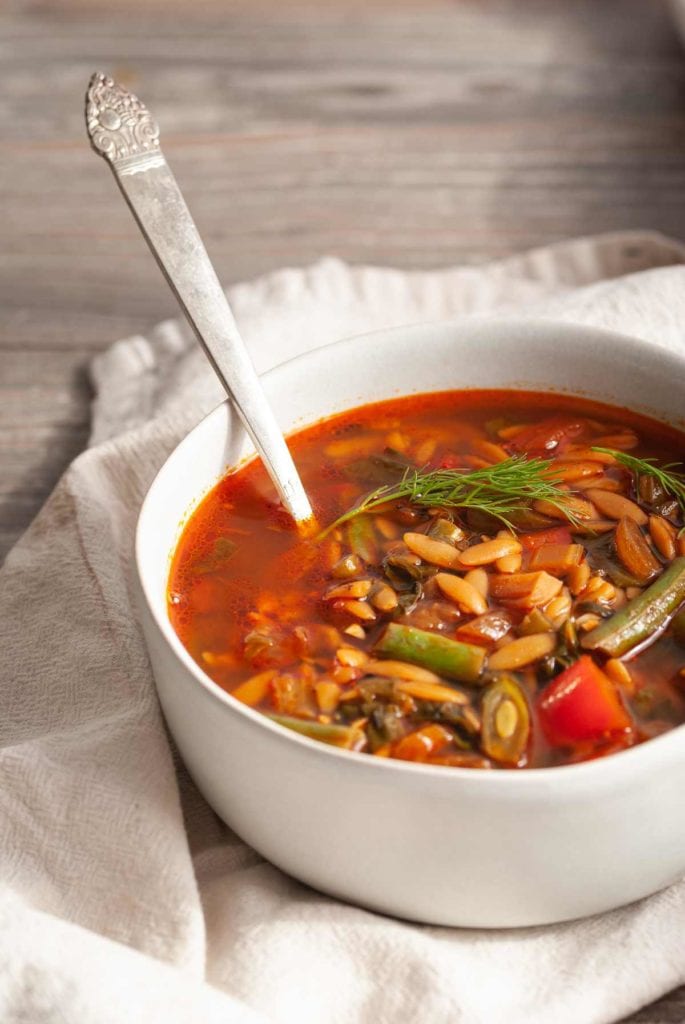 cropped soup bowl with vegan orzo soup and a spoon
