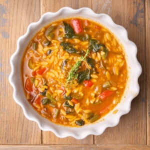 Close up of scallop-edged shallow bowl full of vegetable orzo zoup.