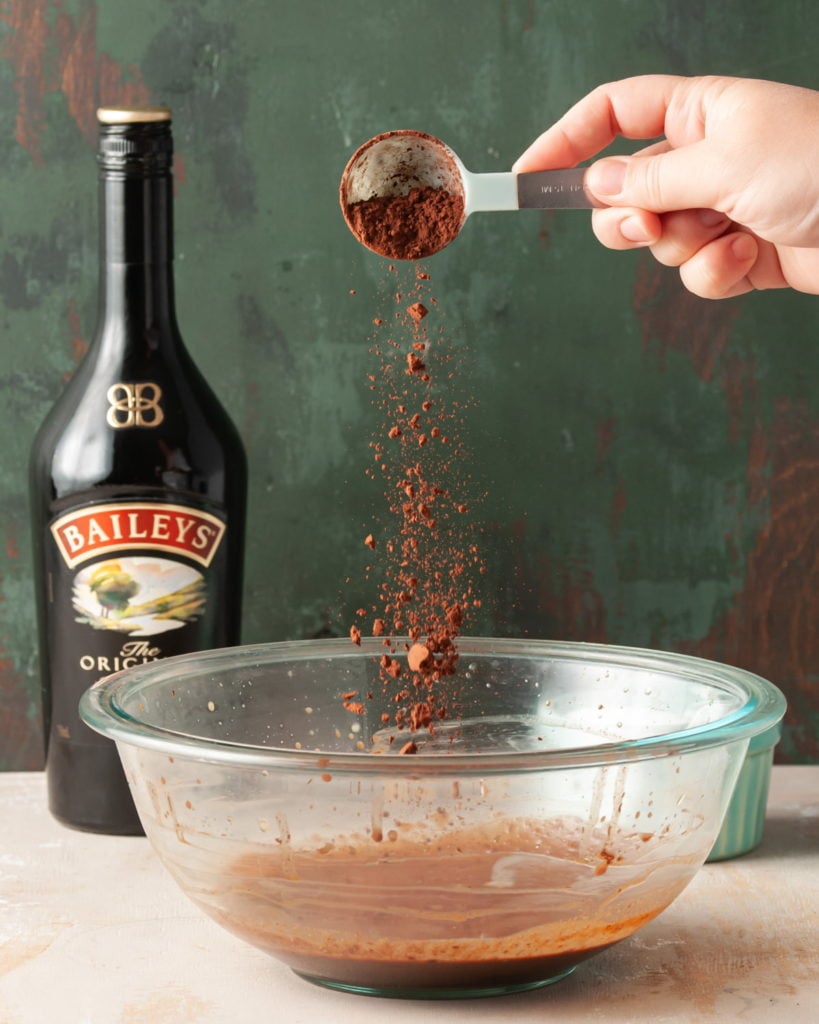 adding cocoa powder to large mixing bowl with Baileys and melted chocolate
