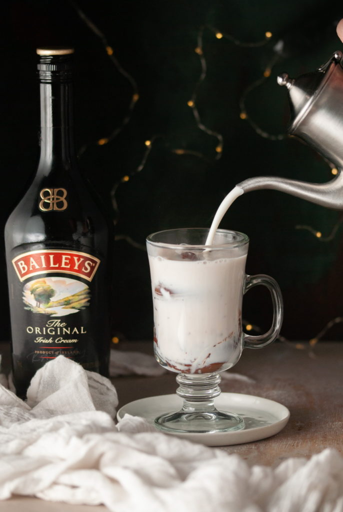 pouring hot milk over Baileys Hot Chocolate Bombs in a glass