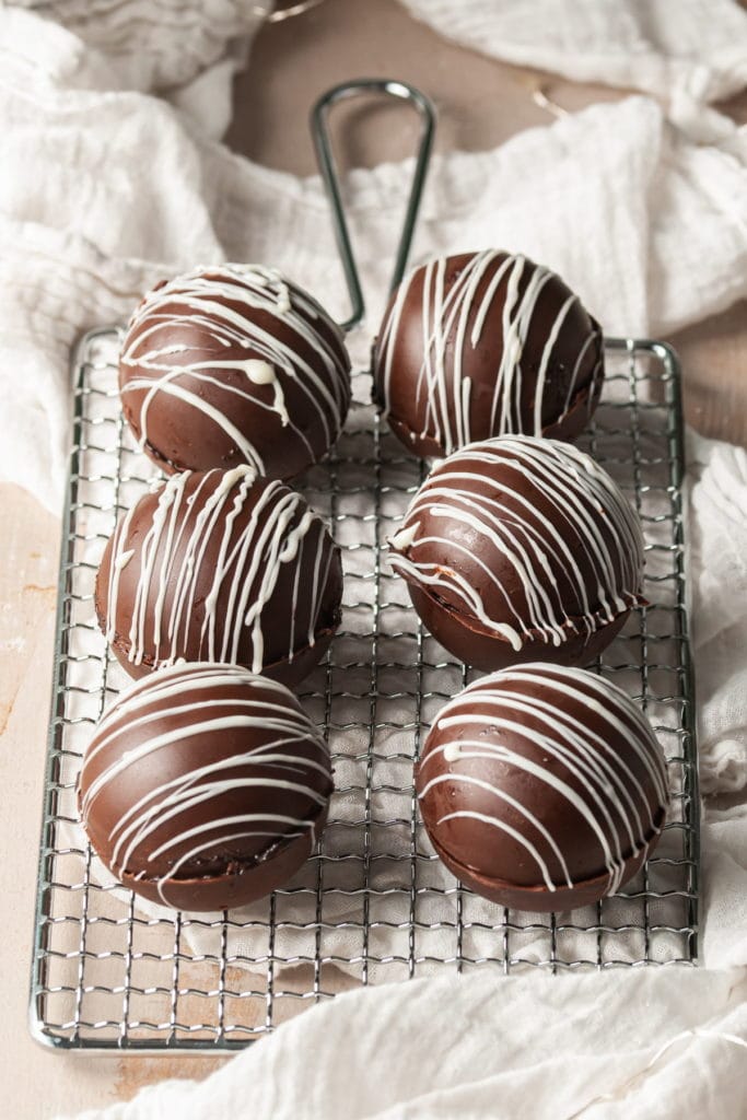 6 Bailey's Hot Chocolate Bombs lined up on a cooling rack drizzled with white chocolate