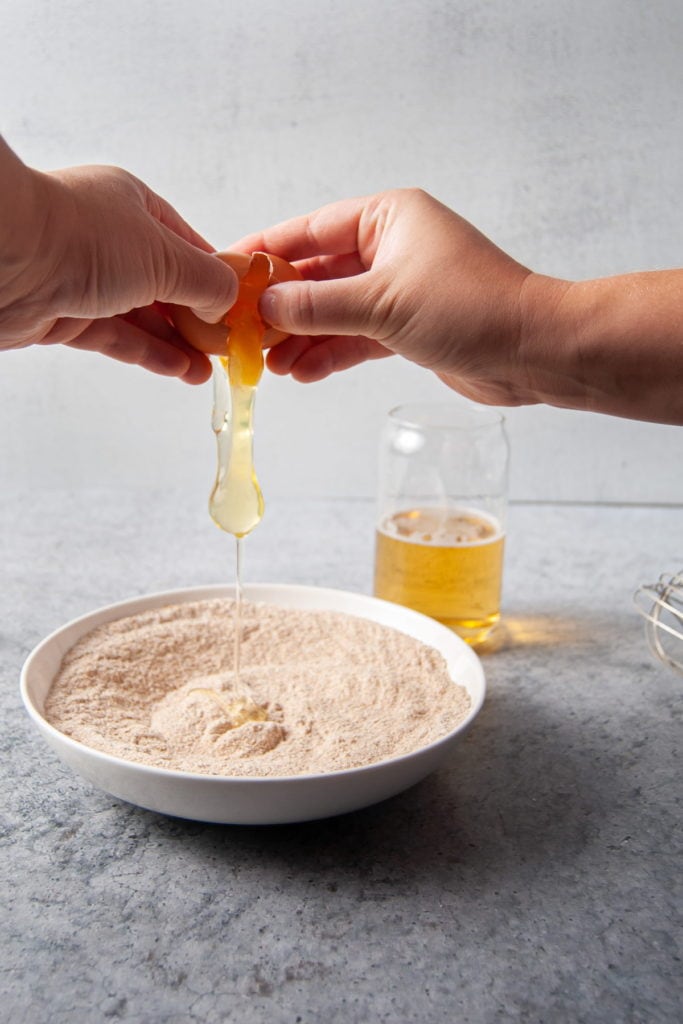 Cracking egg into flour to form fish fry batter.