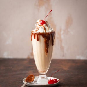 Butterscotch milkshake garnished with dripping butterscotch, whipped cream, and a cherry