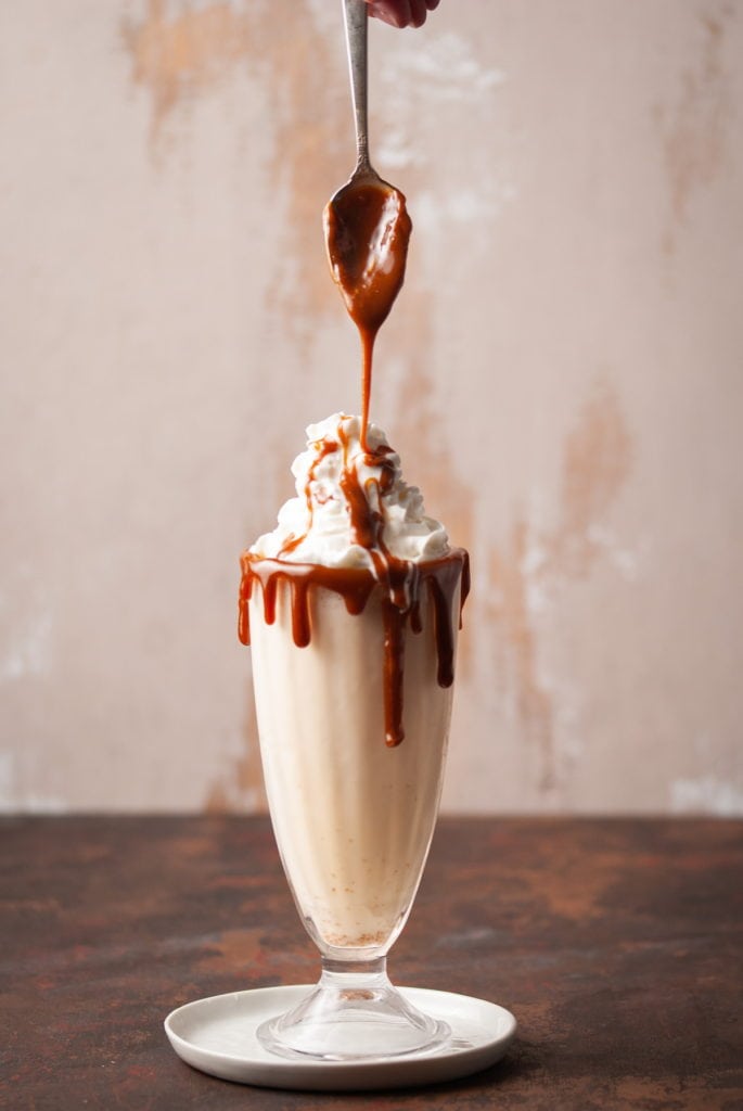butterscotch dripping off of a spoon onto a milkshake
