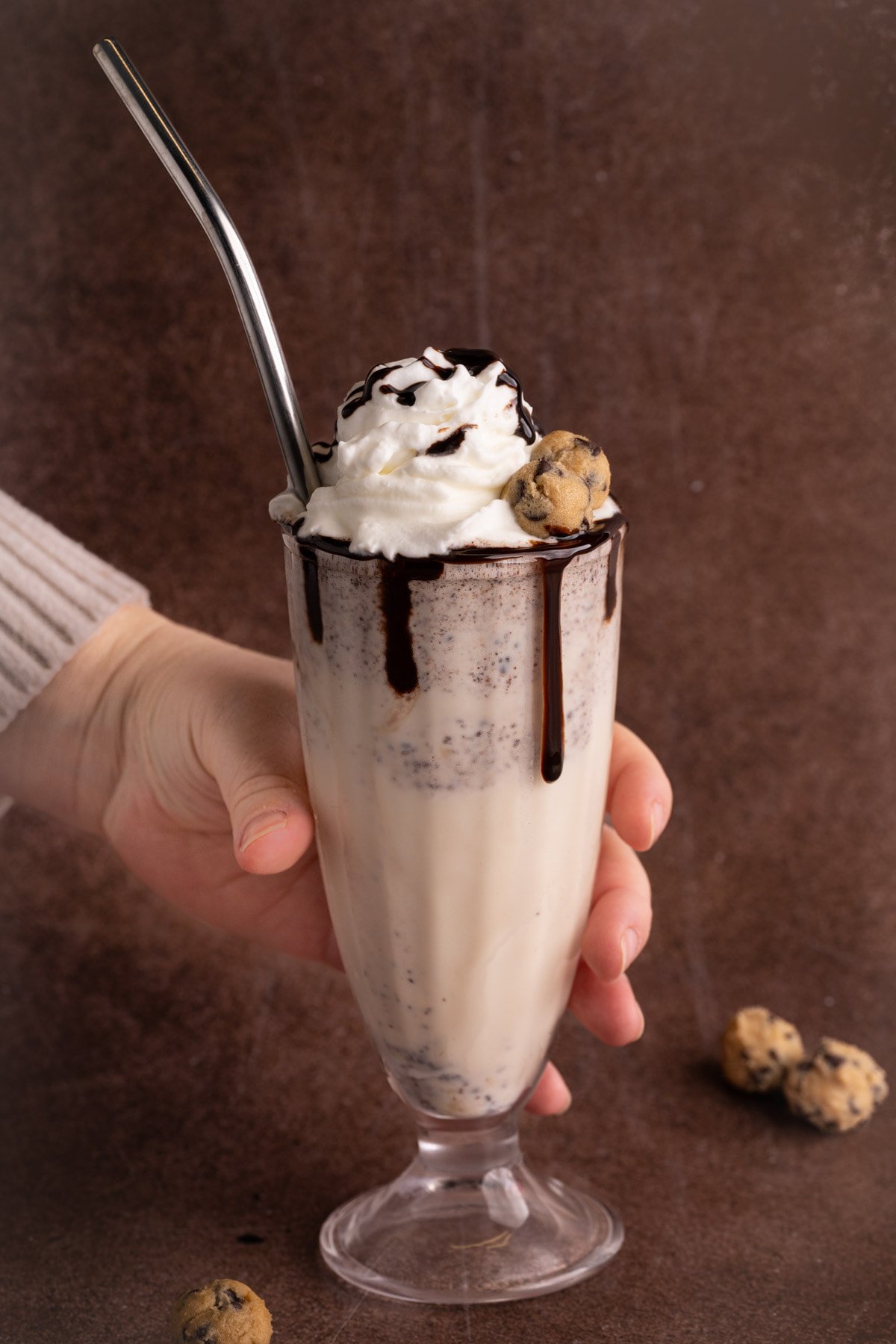 Hand reaching in from the left of the frame to grab cookie dough milkshake.