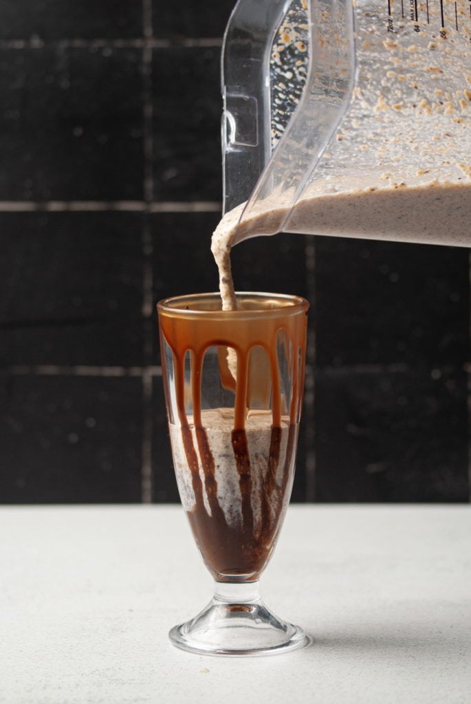 Pouring milkshake into glass with chocolate syrup dripping down the sides