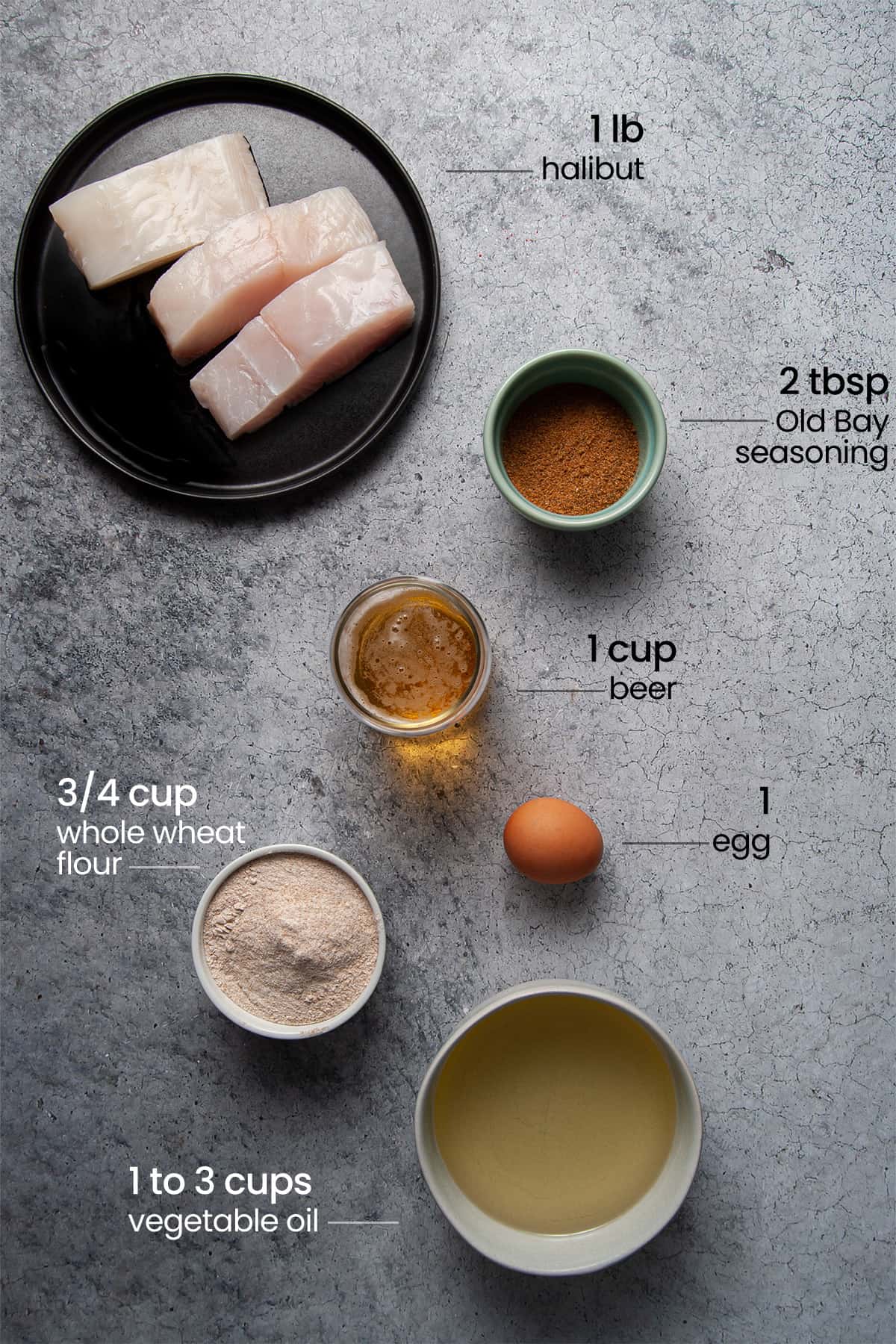 Overhead view of all ingredients for beer battered halibut - halibut, old bay seasoning, beer, egg, flour, and vegetable oil.