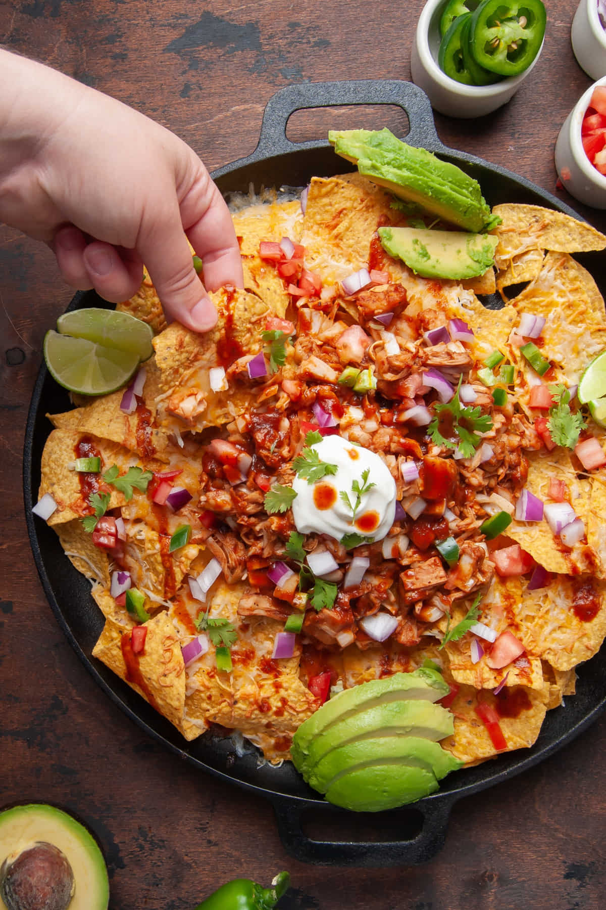 Grabbing a loaded nacho from a colorful plate of Vegetarian BBQ Jackfruit Nachos.