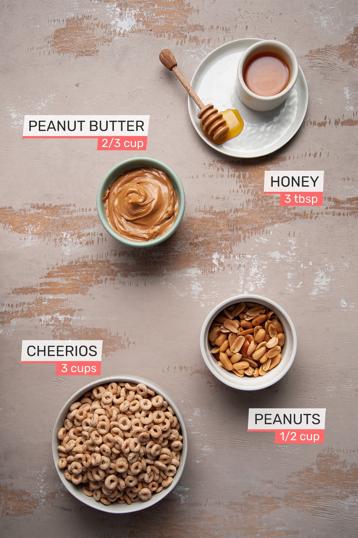overhead view of all ingredients needed for peanut butter cheerio bars on a light wood background - honey, peanut butter, peanuts, cheerios