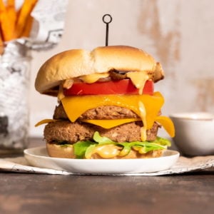 stacked double jackfruit burger with cheese, arugula, tomato, caramelized onion, and sauce