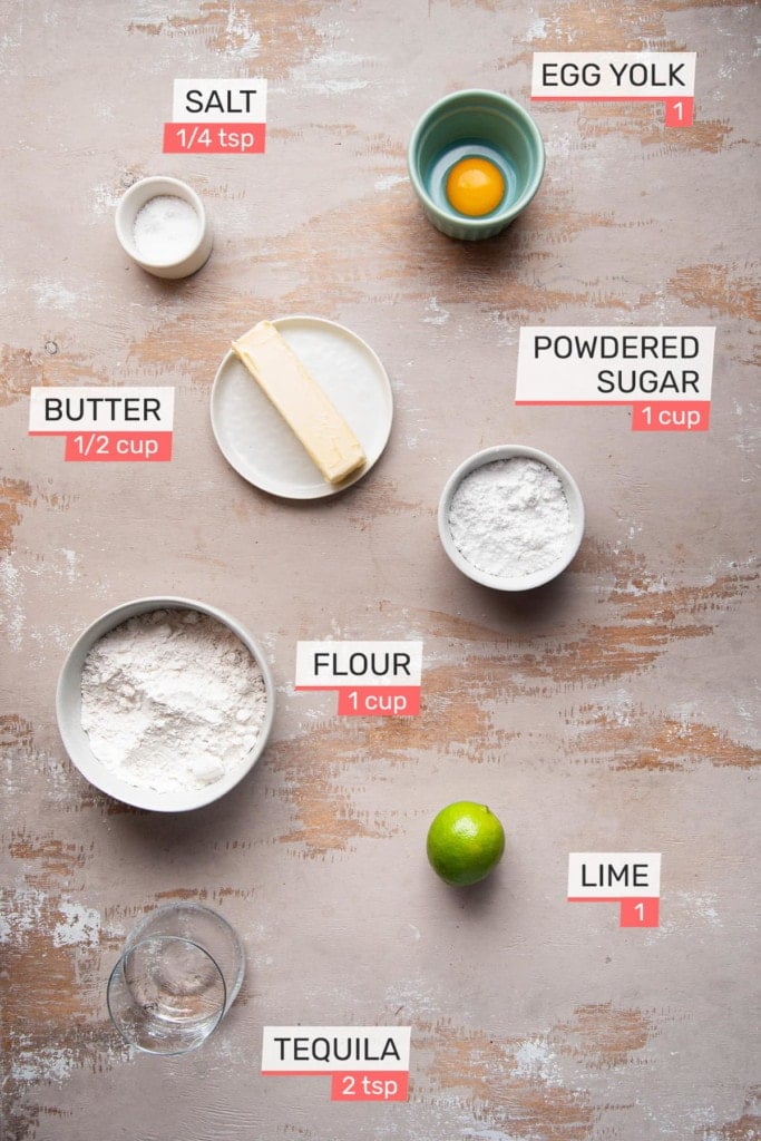 Overhead view of all ingredients needed for Margarita Cookies with Tequila Lime Glaze - egg yolk, salt, butter, powdered sugar, flour, lime, tequila