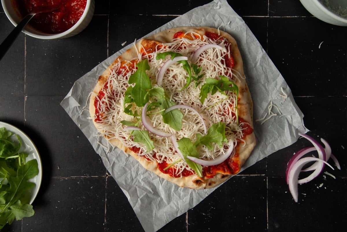 Adding red onion and arugula to breakfast pizza.