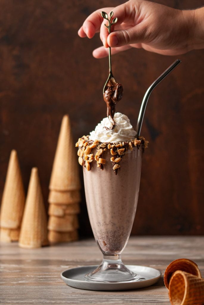 A spoonful of Nutella being dropped on top of whipped cream on a Nutella milkshake