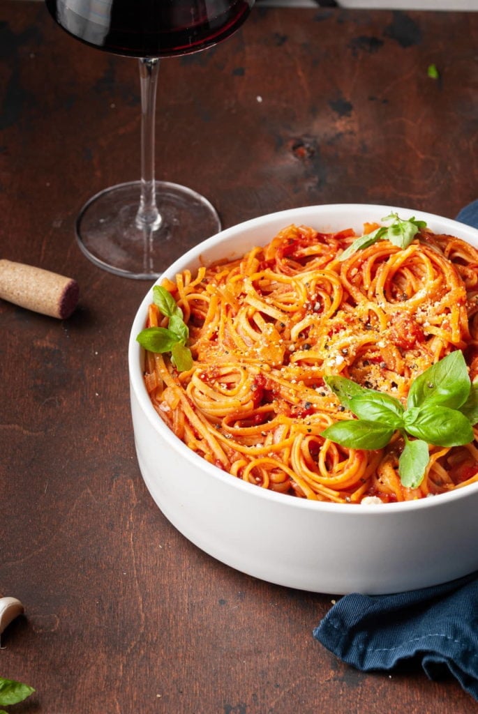 cropped serving bowl with pasta with tomato sauce and glass of wine