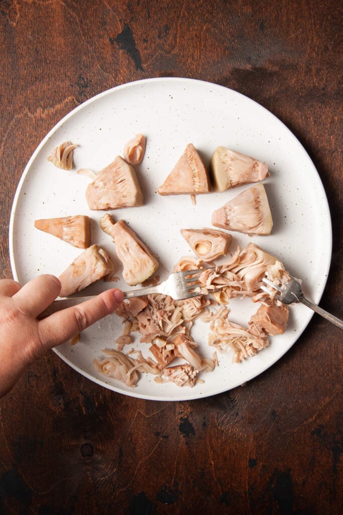 Using forks to pull apart tender boiled jackfruit.