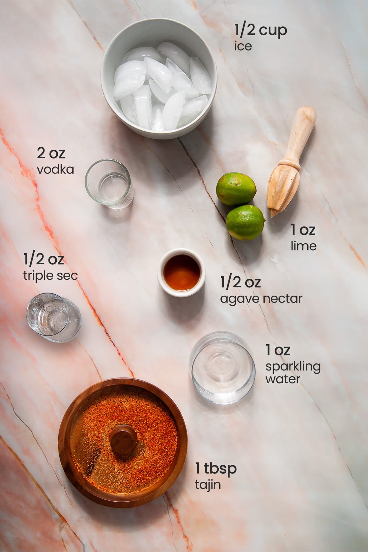 Overhead view of the ingredients needed for sparkling vodka margarita - ice, limes, vodka, agave nectar, sparkling water, and tajin.