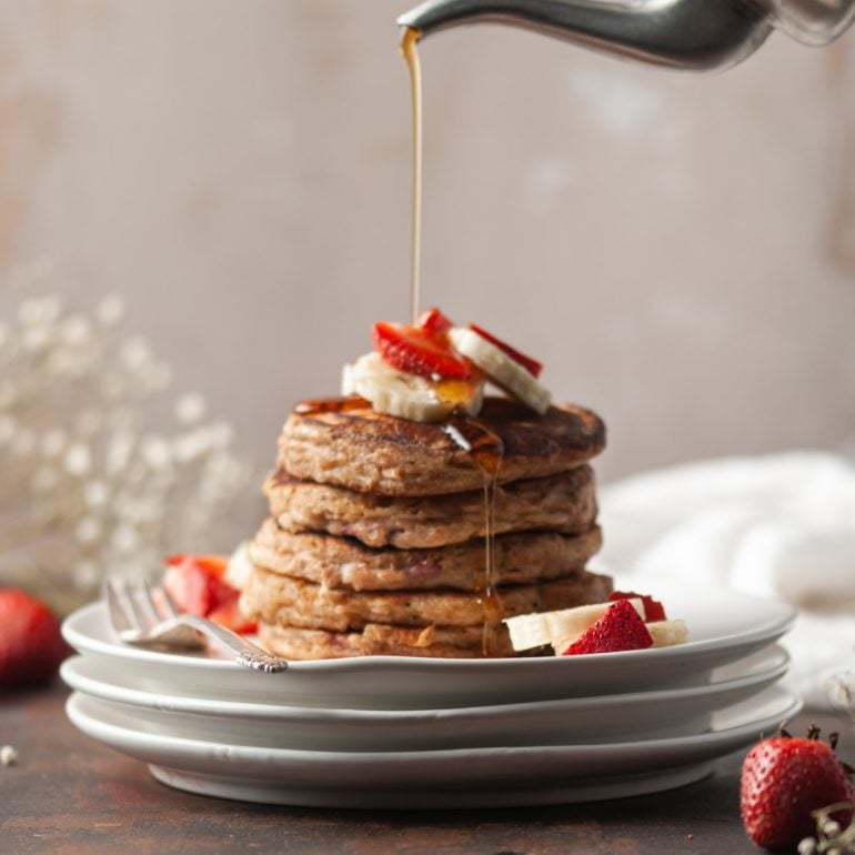 stack of whole wheat strawberry banana pancakes with syrup being poured on top