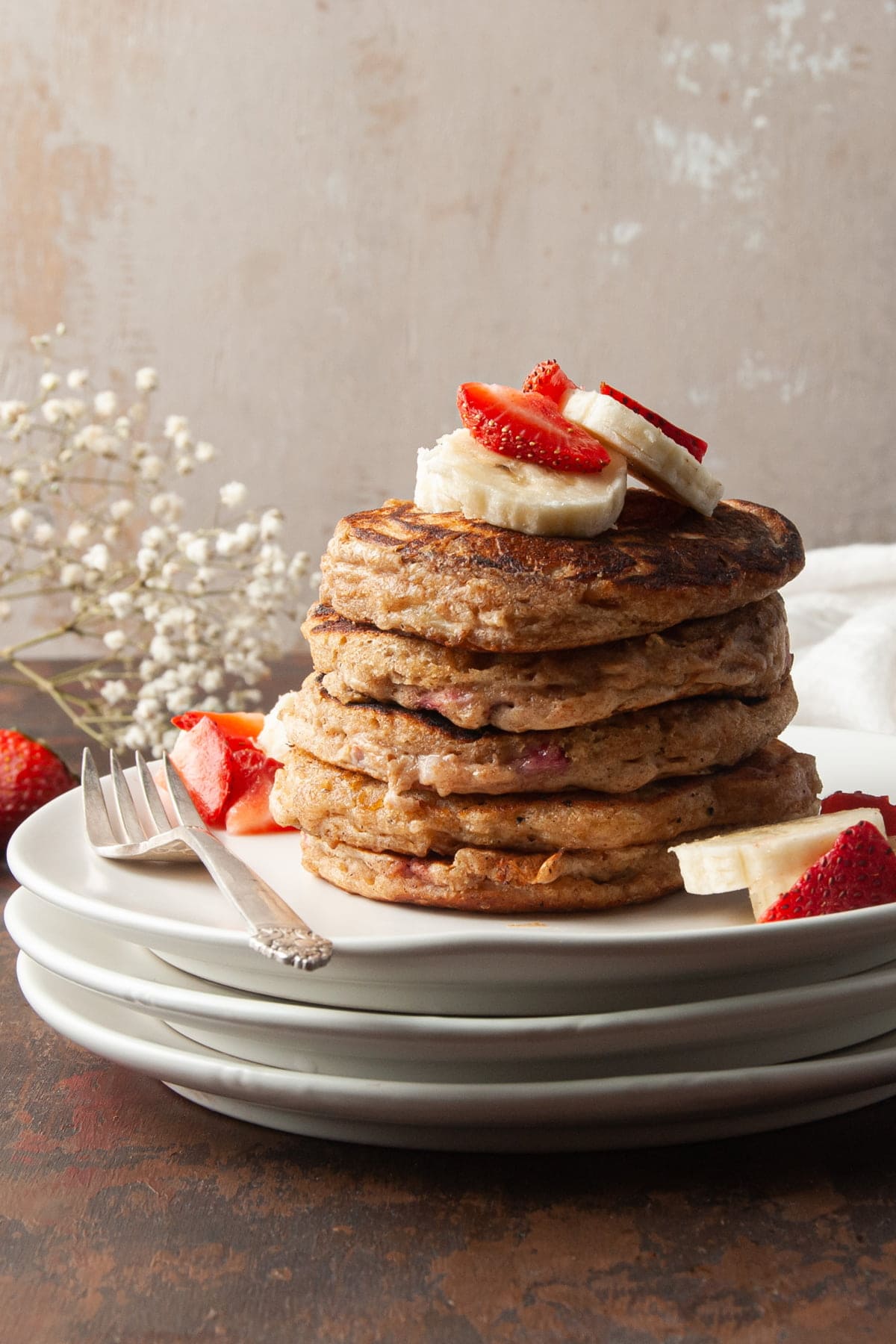 Tall stack of whole wheat pancakes topped with bananas and strawberries.