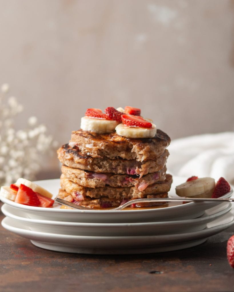 stack of strawberry banana pancakes with forkful taken out of front