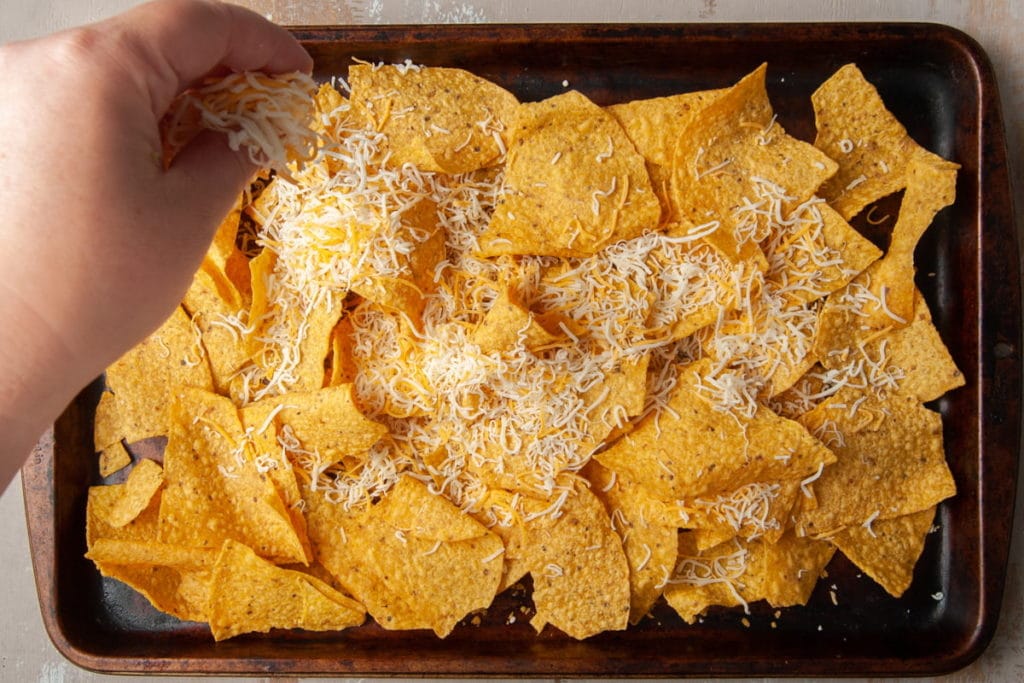 Adding shredded cheese to chips on sheet pan