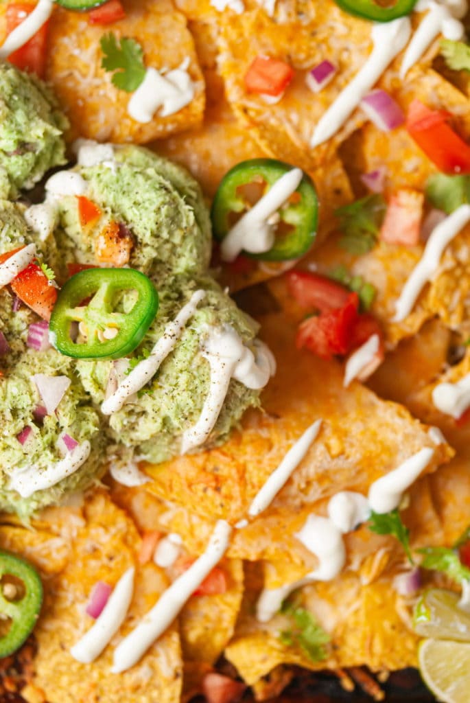 close up of crispy cheesy nachos with avocado and tuna and drizzled with sour cream