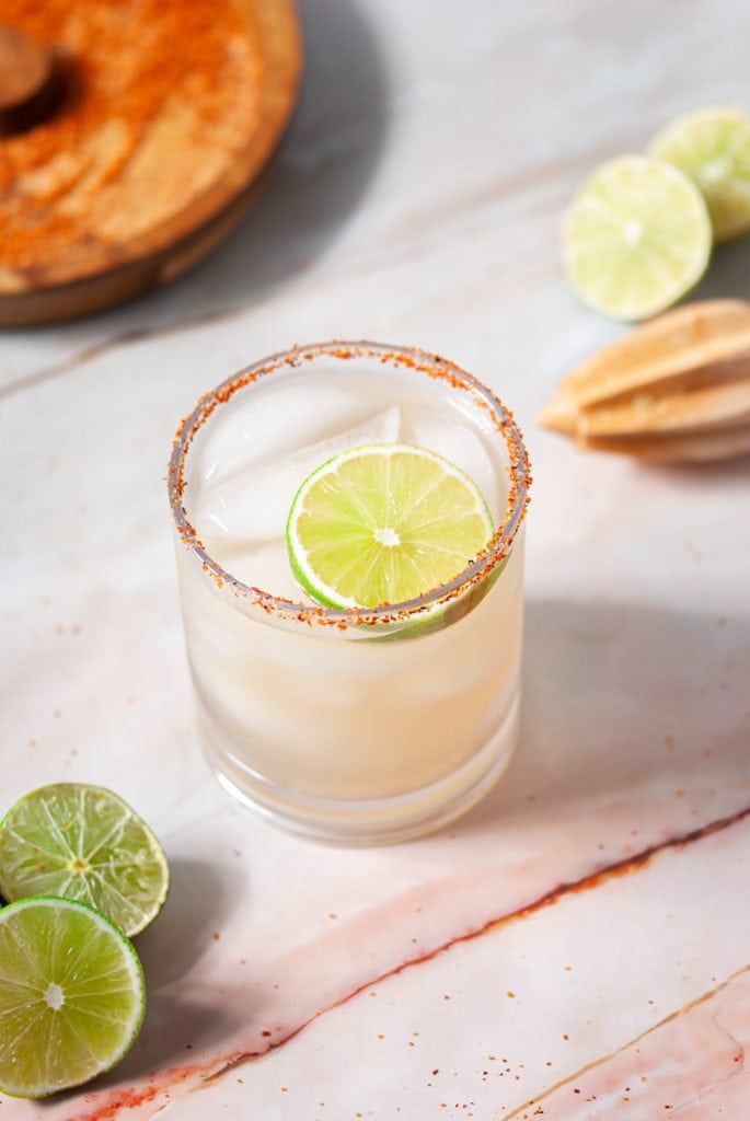 vodka margarita surrounded by juicer, limes, and cocktail rimmer