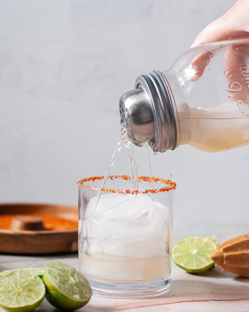 pouring vodka margarita from a shaker into a glass with ice