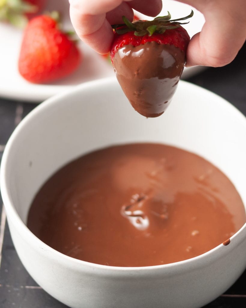 dipping a strawberry into melted dark chocolate