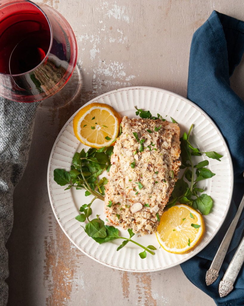 hand grabbing wine next to plate of salmon