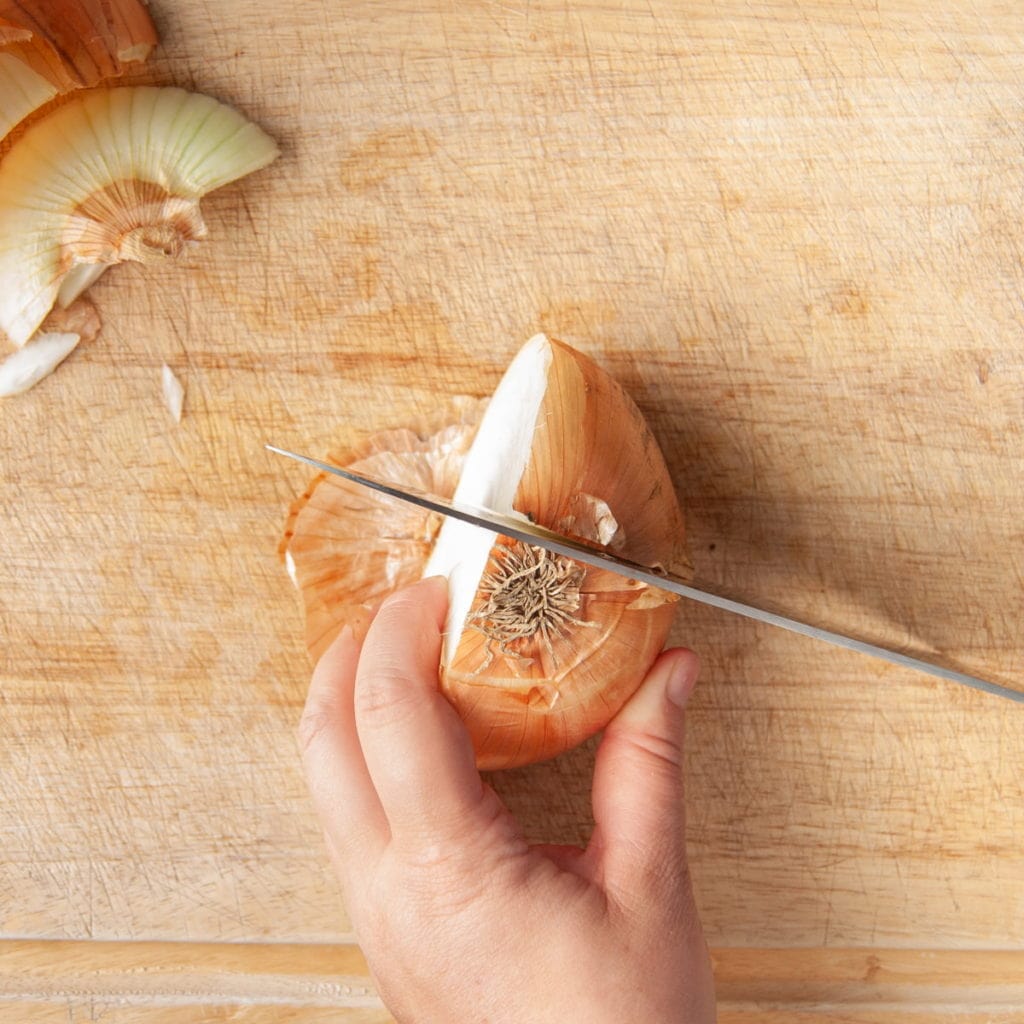 Cutting into half of an onion next to the bulb
