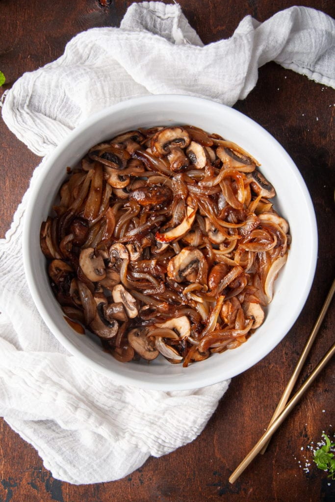 caramelized onions and mushrooms in a serving bowl with gold serving utensils