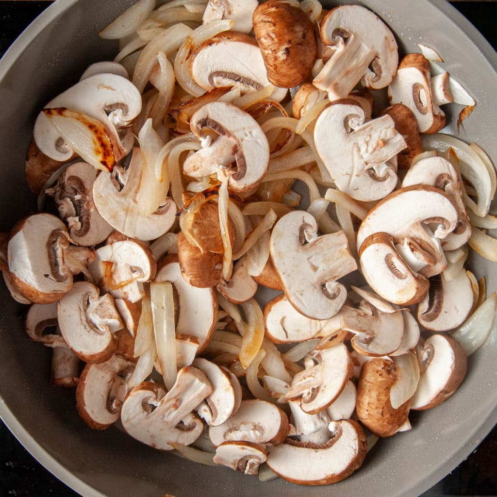 mixing sliced mushrooms into stir fried onions