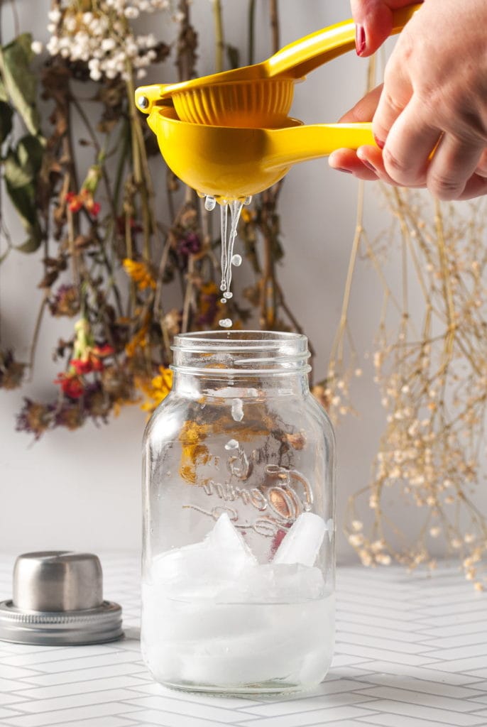 squeezing lemon juice from a lemon into a cocktail shaker