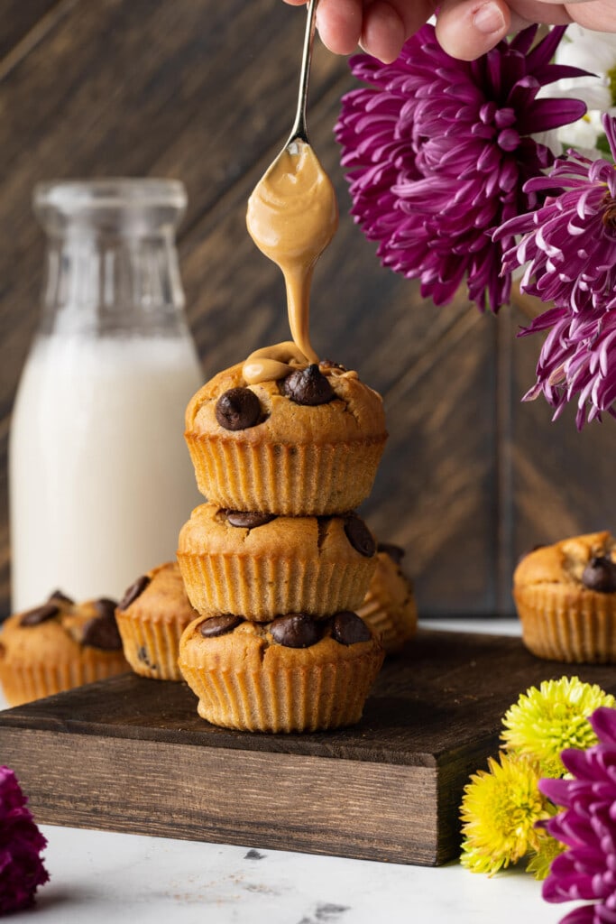 Dripping peanut butter onto stack of muffins with chocolate chips