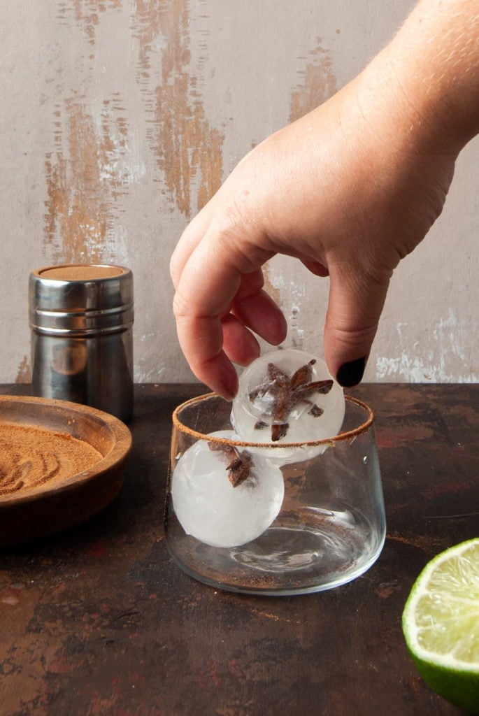 adding ice with star anise frozen inside of it to a rimmed margarita glass