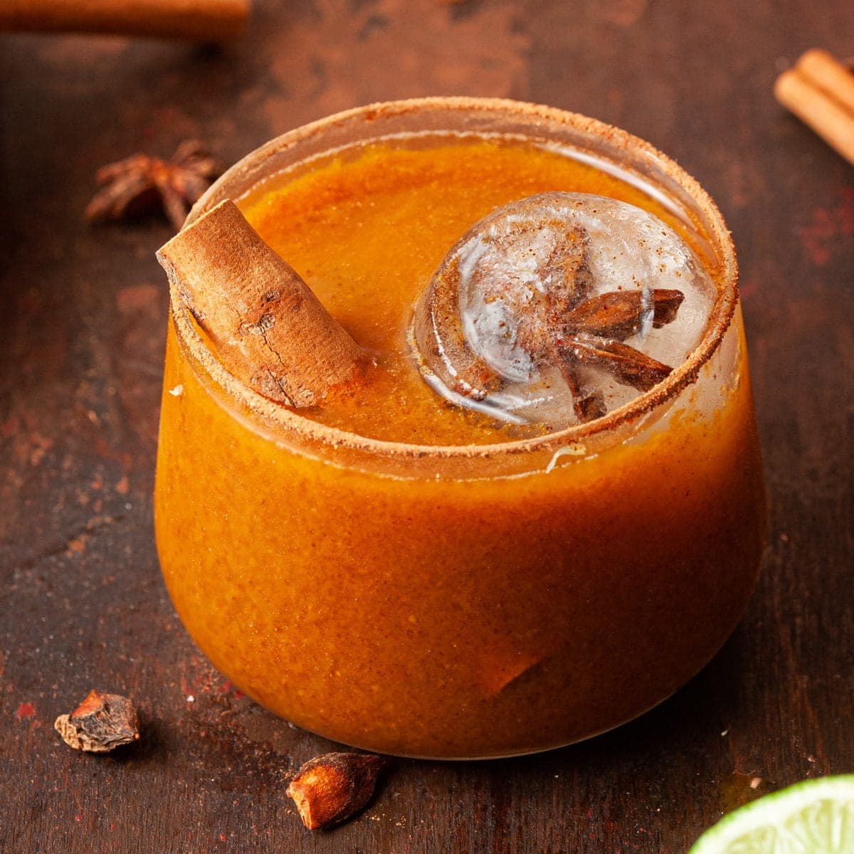 fall margarita in a pumpkin spice rimmed glass and garnished with a cinnamon stick and lime